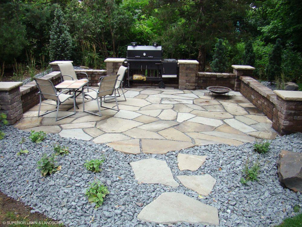 A stone patio with a grill and chairs on it