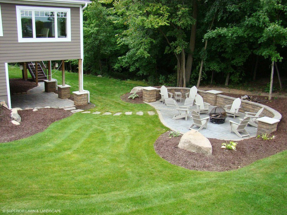 A backyard with a fire pit and chairs in front of a house.