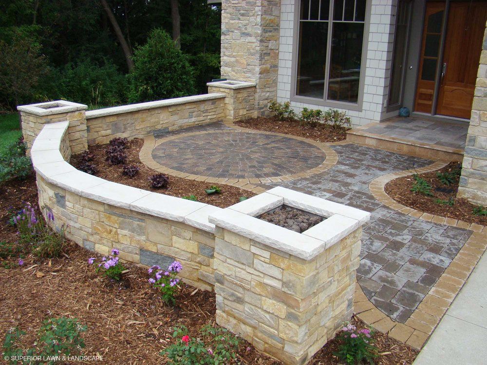 A stone wall surrounds a circular patio in front of a house.