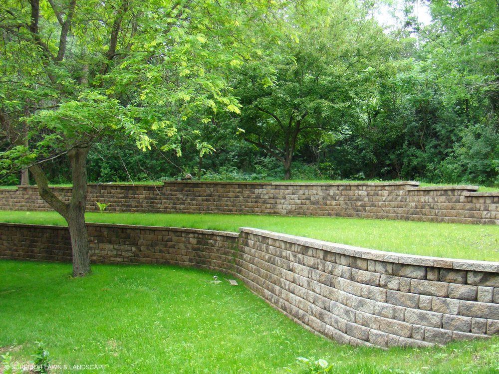 A brick wall surrounds a lush green field with trees in the background.