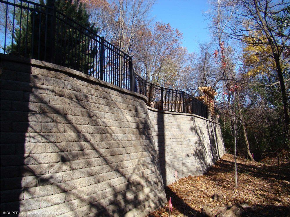 A brick wall with a metal fence surrounding it and trees in the background.