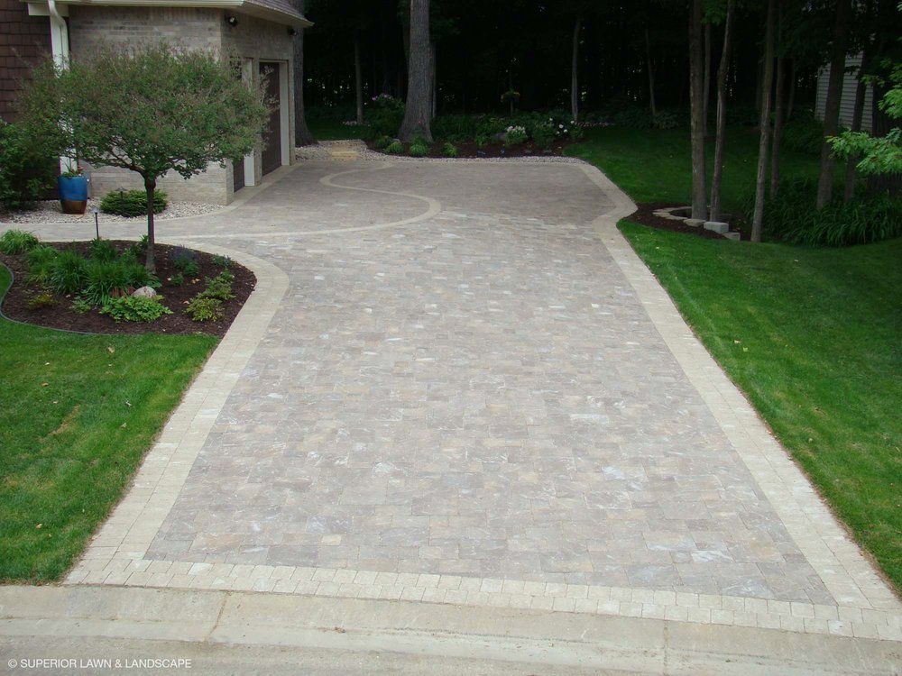 A brick driveway leading to a house with a lush green lawn.