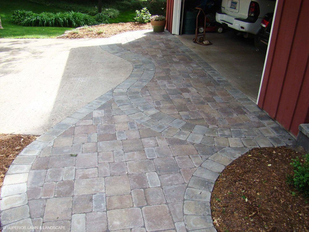 A brick walkway leading to a garage with a car parked in it.
