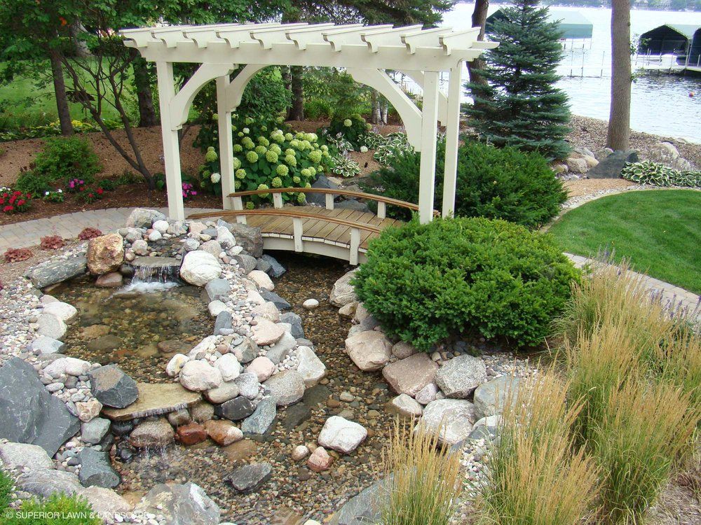 A garden with a pergola and a bridge over a pond