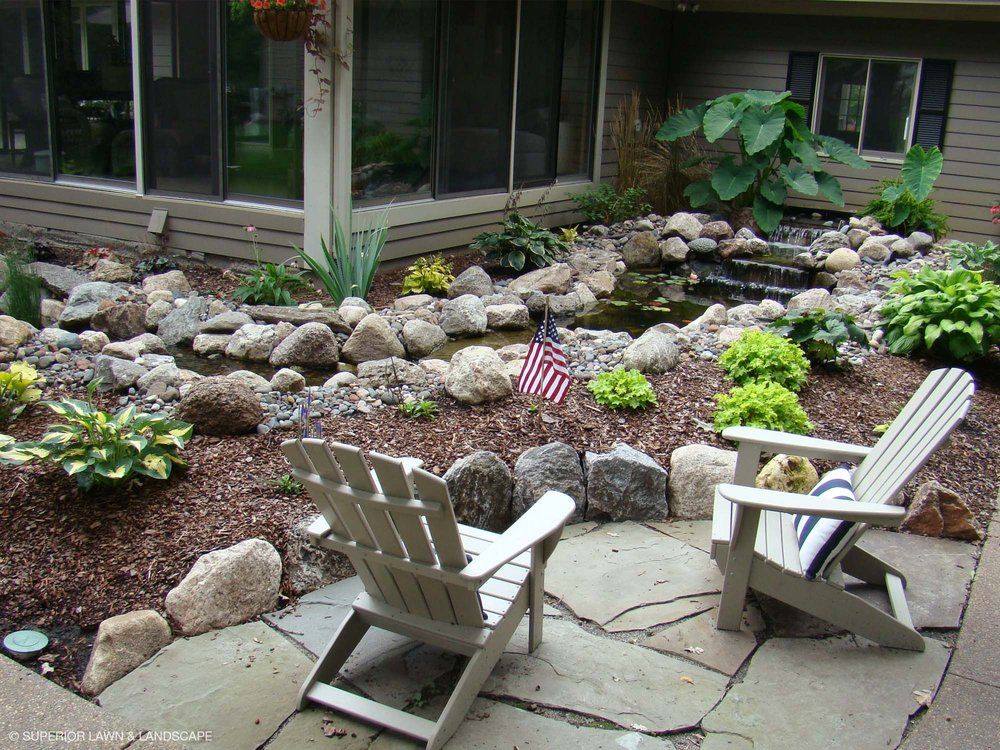 A patio with two chairs and a pond in the background