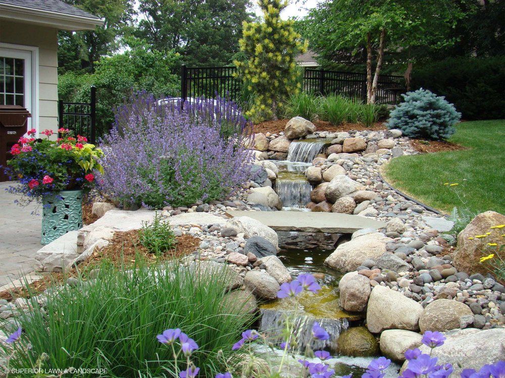 A garden with purple flowers and a waterfall