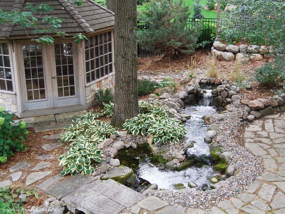 A pond with a waterfall and a gazebo in the background