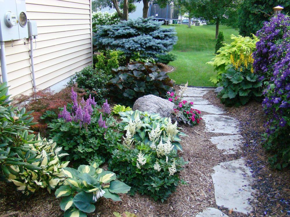 A stone walkway surrounded by flowers and shrubs leading to a house