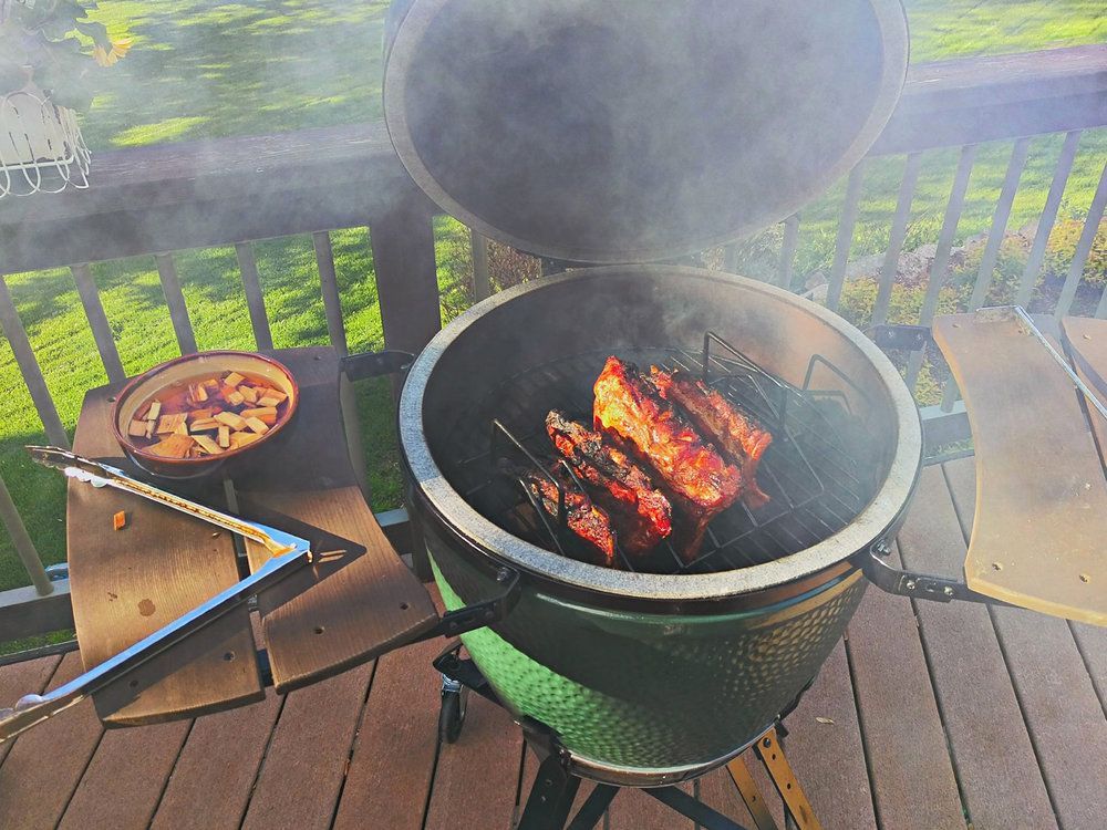 Meat is cooking on a grill on a wooden deck.