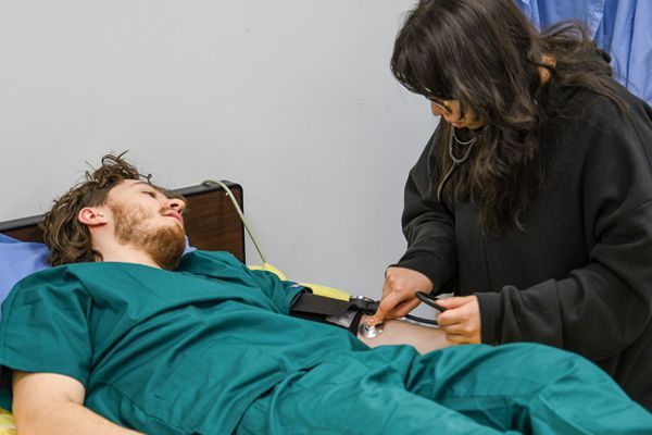 Person in scrubs on bed, being examined by person with stethoscope.