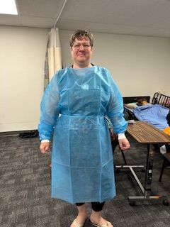 Woman in blue medical gown, standing indoors, likely in a healthcare setting.