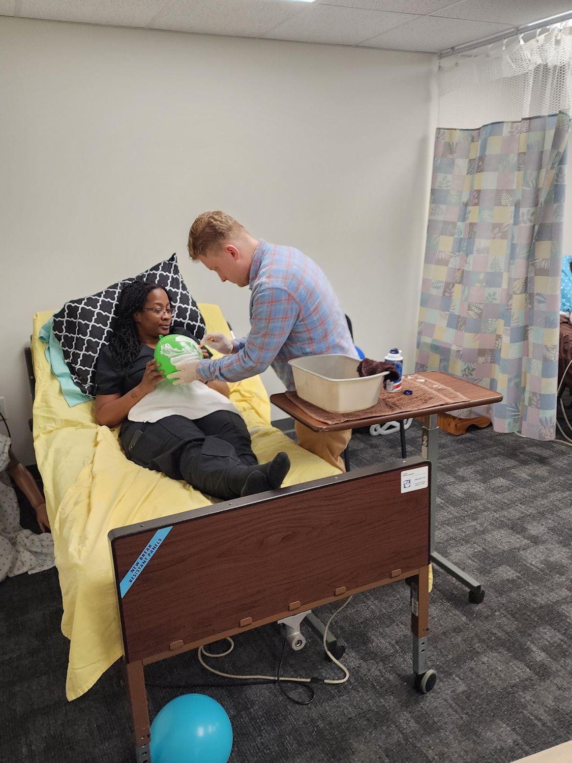 A person is in bed, being assisted by another medical trainee.