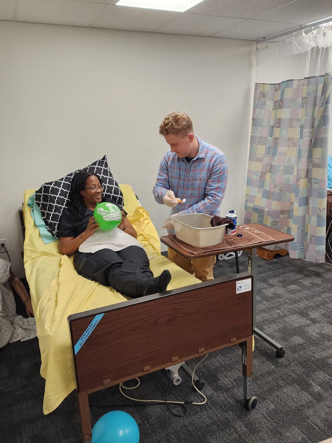 A man in training feeds a woman in a bed.