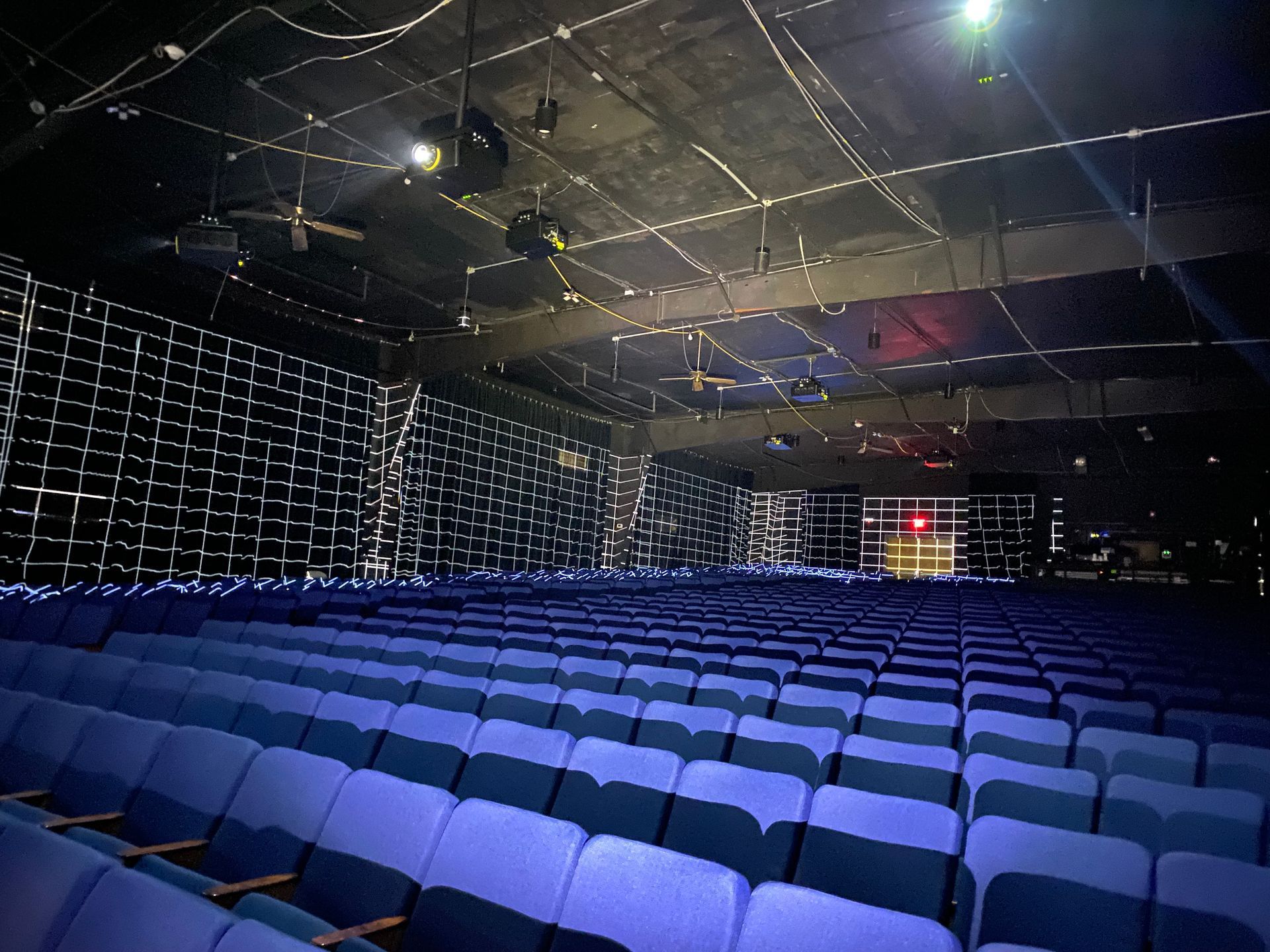 Empty theater auditorium with blue seating. Black ceiling and side walls, stage in the distance.