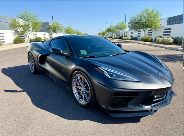 Black sports car parked on a sunny street with modern buildings in the background