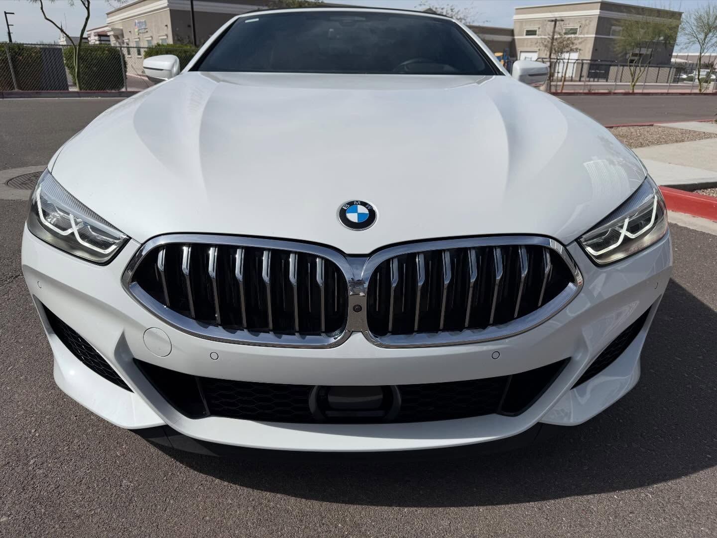 Front view of a white BMW sports car parked on a street under bright sunlight