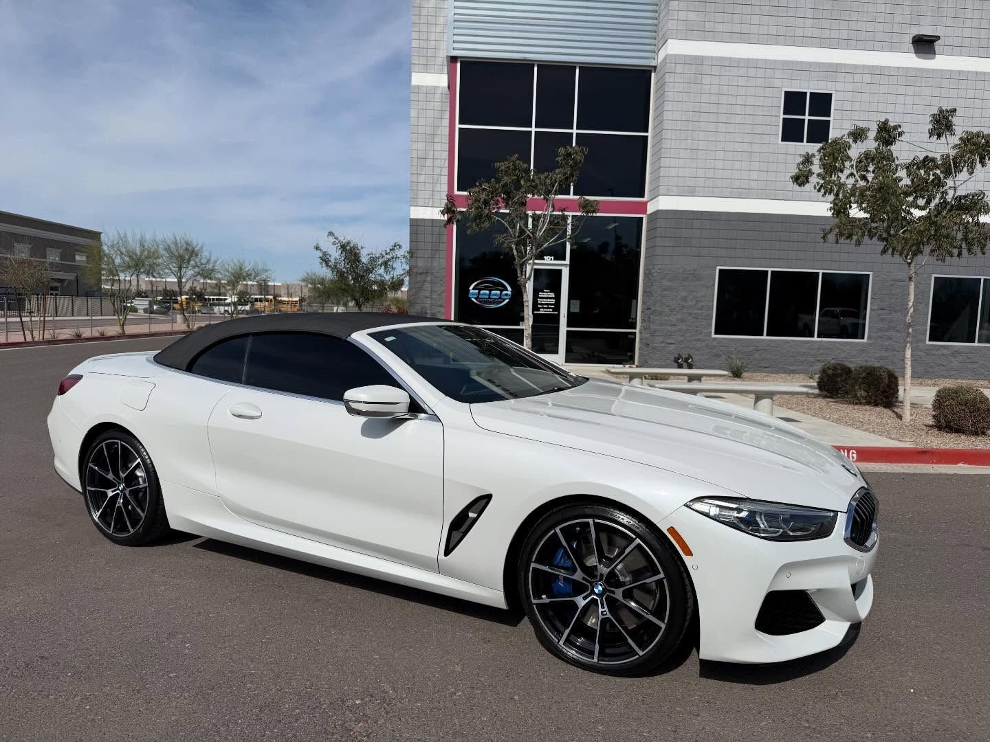 White sports sedan parked outside a modern building on a sunny day