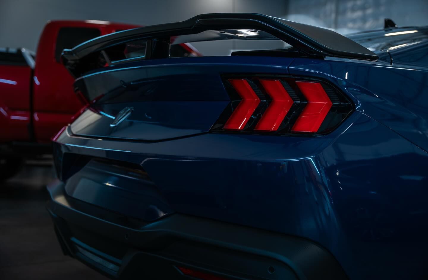 Blue sports car rear with red taillights in a dimly lit garage