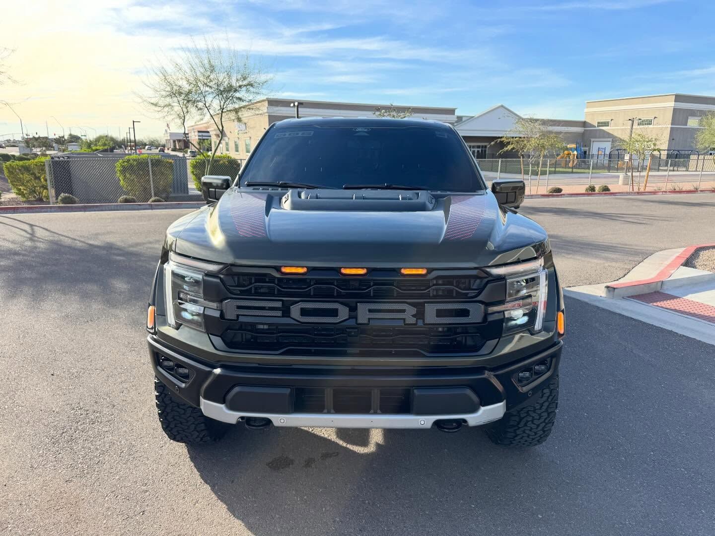Black pickup truck facing forward in a parking lot with orange lights on the grille and a hood scoop