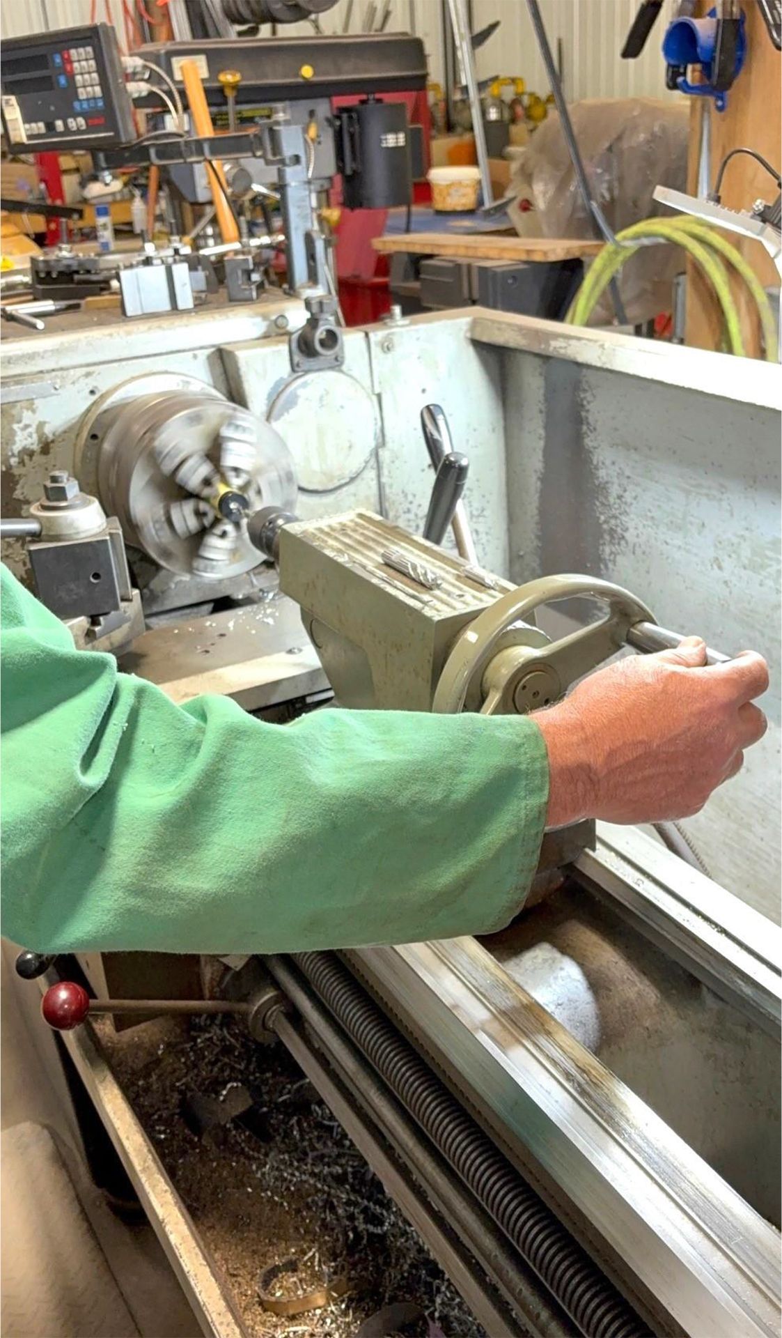 A man in a green shirt is using a lathe in a workshop