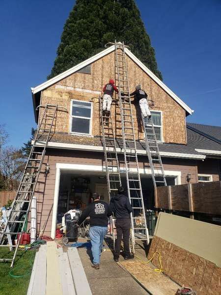 Three workers on ladders, siding a house, two on the roof, two on ground.