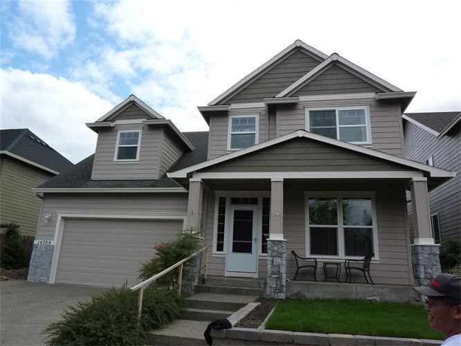 Tan two-story house with beige siding, porch, garage, and lawn. Blue sky background.