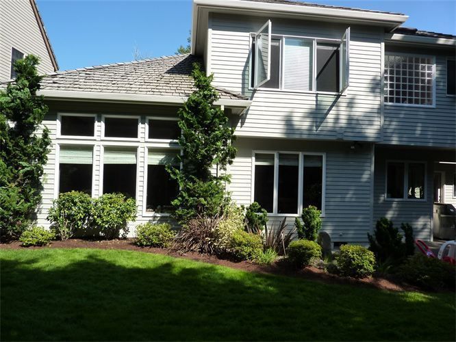 Two-story house with gray siding, white window frames, and a green lawn in sunlight.