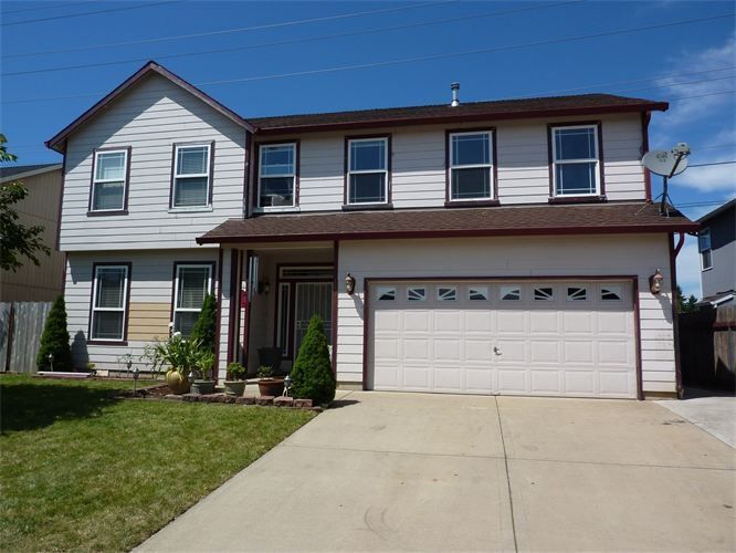 Two-story house with light siding, white garage door, and a concrete driveway on a sunny day.