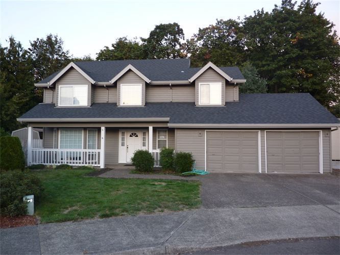 Two-story house with gray siding, dark roof, three garage doors, and a small porch.