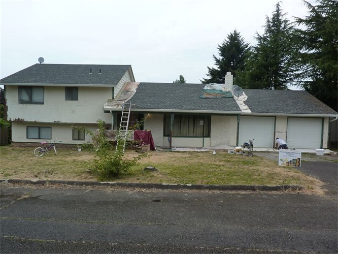 House with roof repairs in progress; ladder, workers, and materials visible. Overcast day.