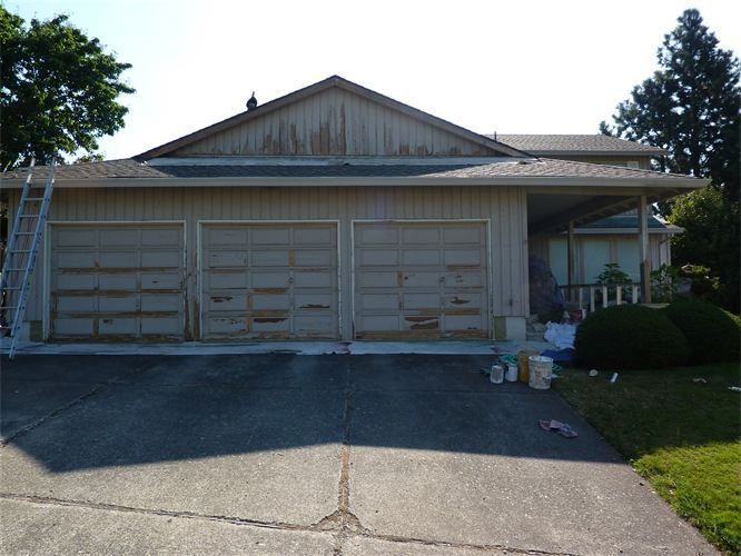 Garage exterior with peeling paint; ladder beside it, driveway in front.