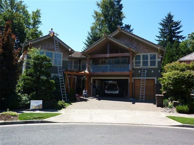 Two-story house with ladders, garage open, and workers painting exterior on a sunny day.