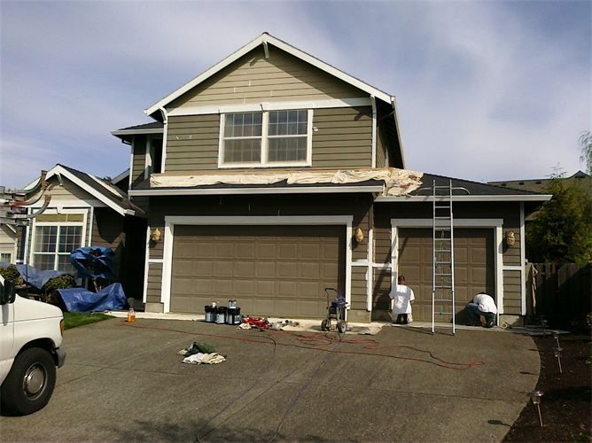 House exterior with garage doors, workers, and ladder.