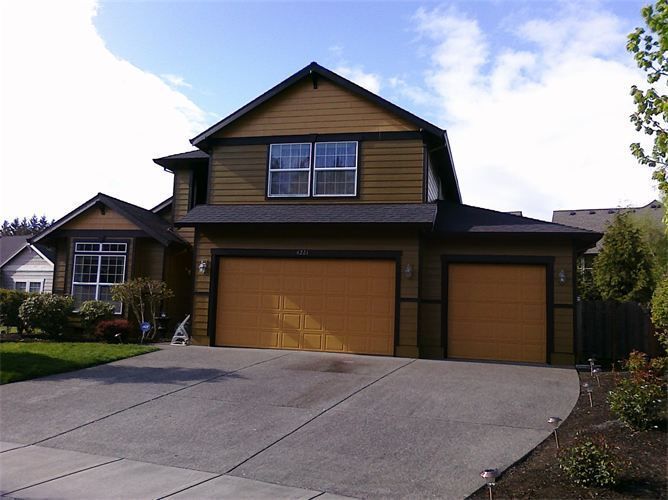 Two-story house with tan siding, two-car garage, and driveway on a sunny day.