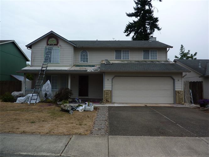 Two-story house with ongoing exterior painting; ladder, tarp, and paint buckets visible. Overcast sky.