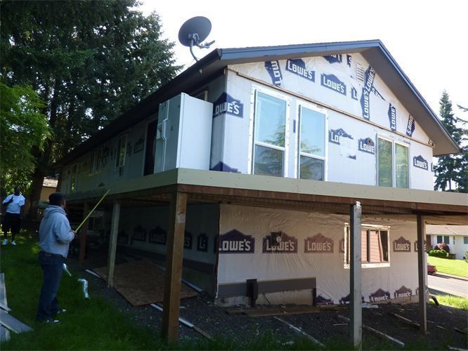 House under construction with new windows and exterior sheathing; two men working outdoors.