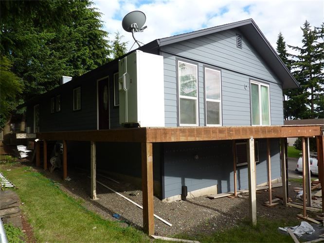 House with gray siding and brown deck being built; a satellite dish sits on the roof.