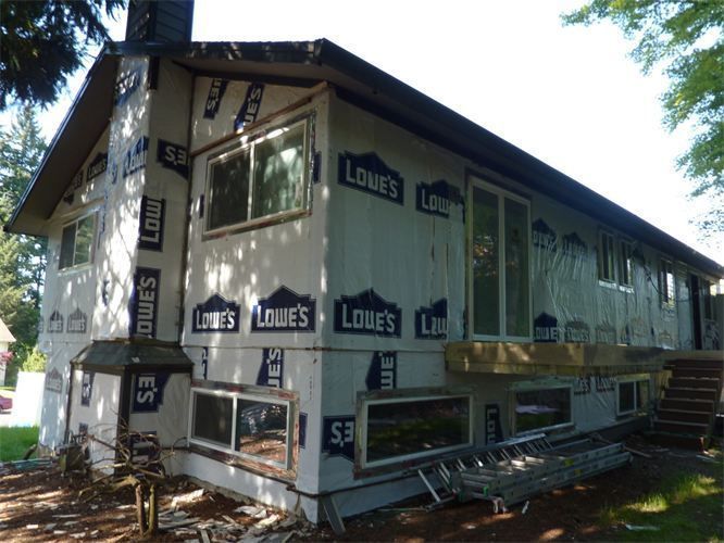 House exterior during renovation; covered in Lowe's weather-resistant barrier, windows exposed.