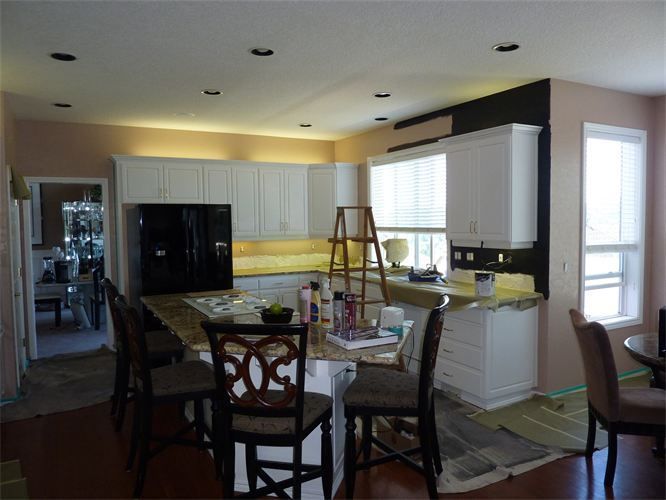 Kitchen interior with white cabinets, black refrigerator, island with bar stools, and open doorway.