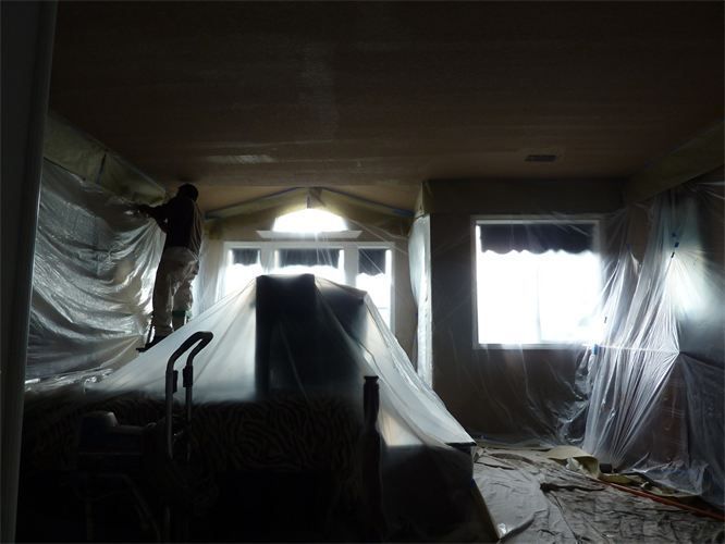 Person painting a ceiling, room covered in plastic sheeting.