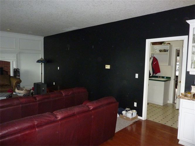 A living room with a red leather sofa, black accent wall, and doorway to a kitchen.