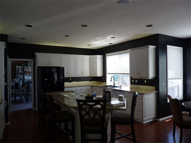 Kitchen with white cabinets, dark walls, granite island, and dark wood floor.