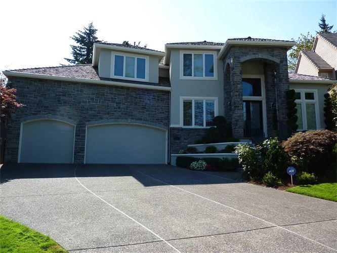 Two-story house with gray stone and stucco exterior, two-car garage, and paved driveway.