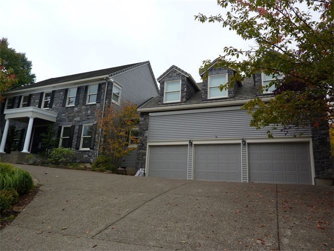 Two-story house with a three-car garage; gray siding, asphalt driveway, overcast sky.