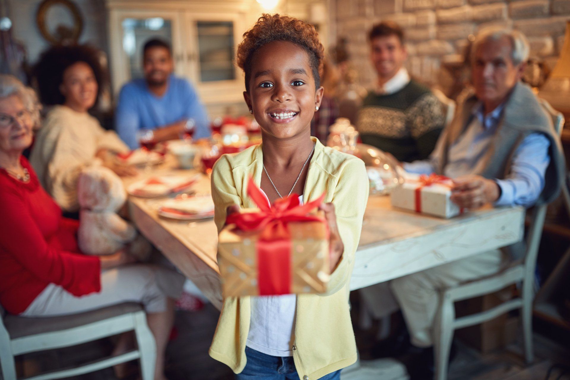 little girl holding wrapped gift and smiling while family looks on in background