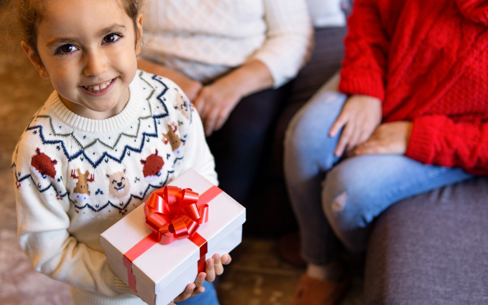 little girl holding wrapped gift and smiling while family looks on in background