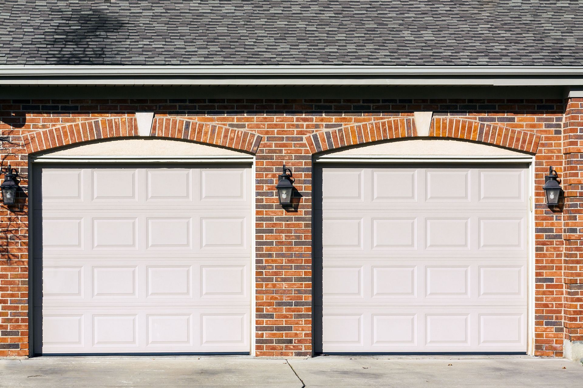 Two white garage doors on a brick house facade