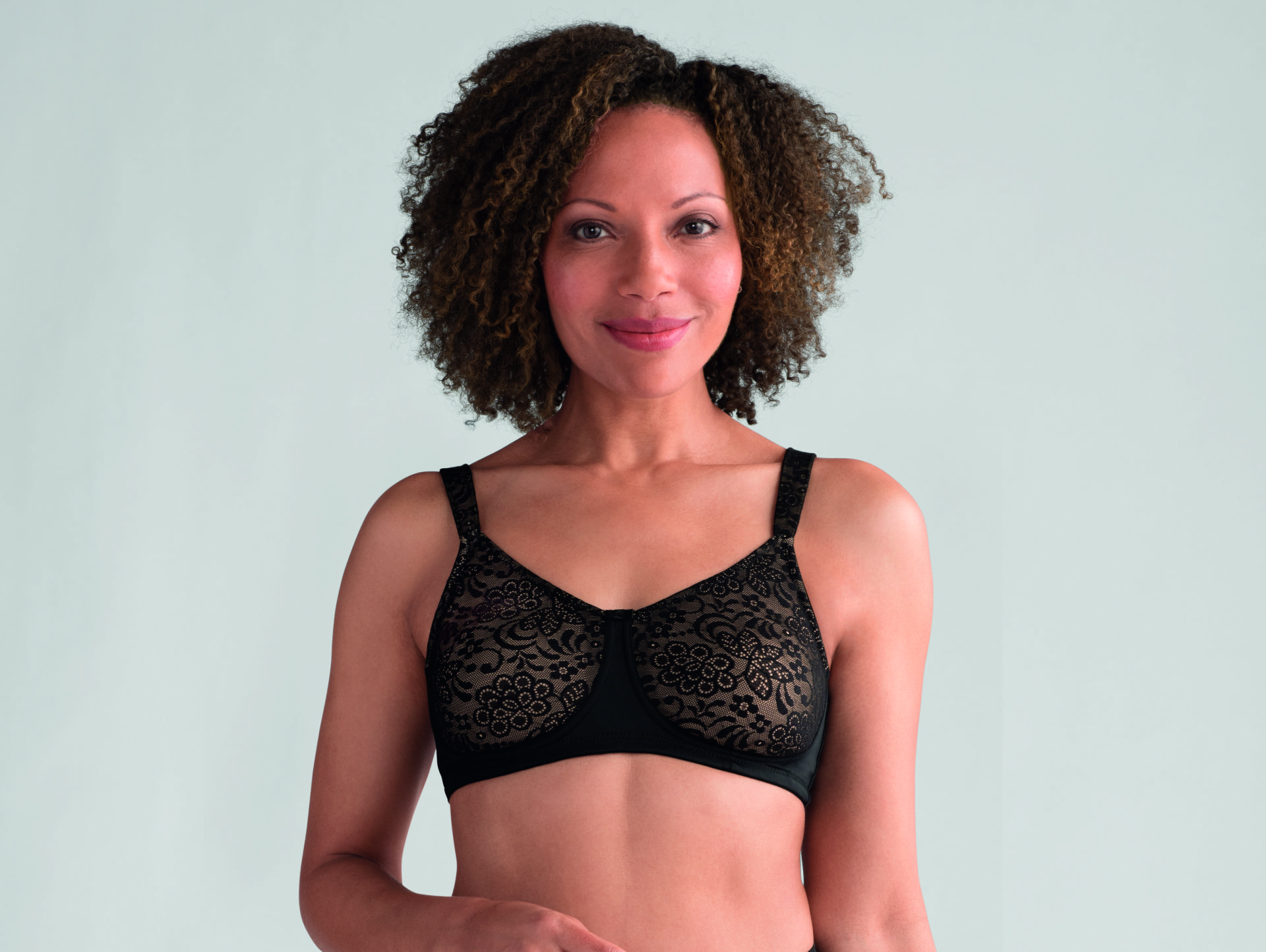 A woman is wearing a black bra and smiling.