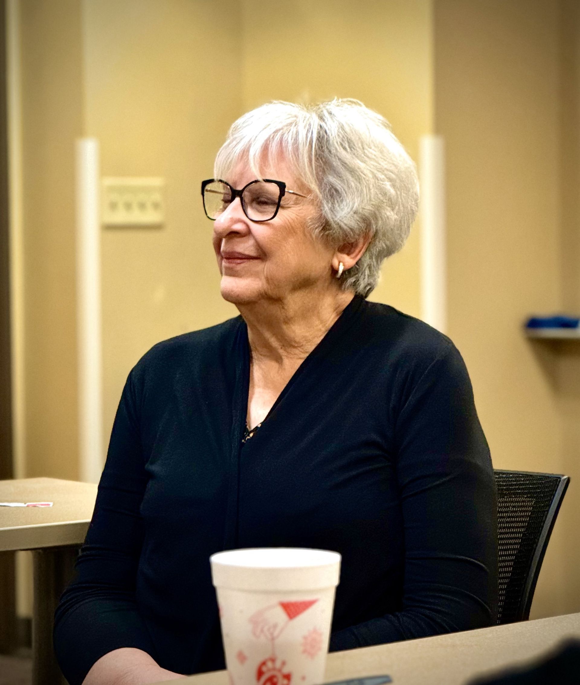 A woman wearing glasses is sitting at a table with a cup of coffee