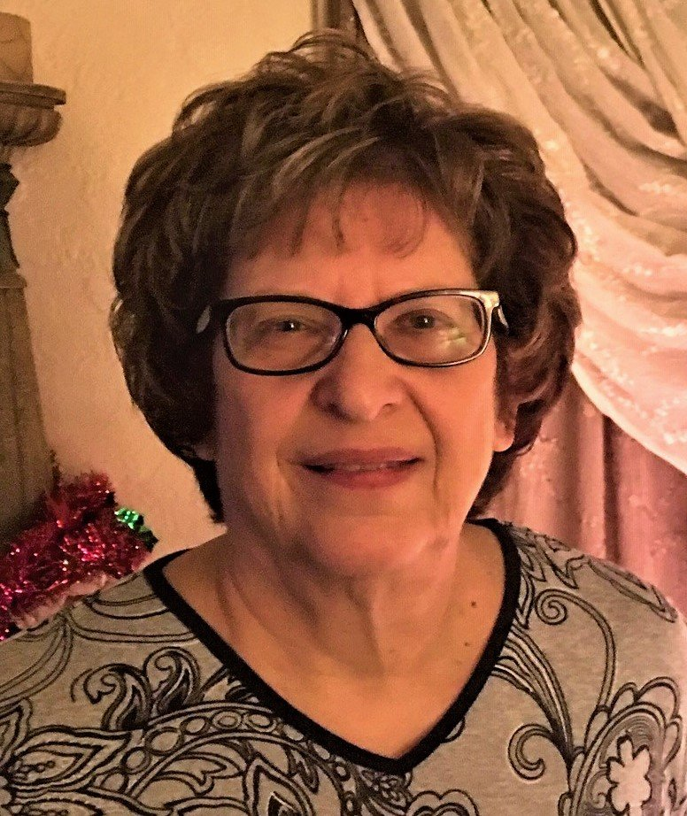 A woman wearing glasses and a floral shirt is smiling for the camera.
